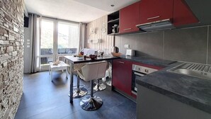 A modern kitchen with red cabinets, a stainless steel range hood, and a dining area with a white table and chairs. - Ski-in/ski-out & foot of the slopes, 5th floor, balcony, tv, 27m², Les Menuires (Les Menuires)