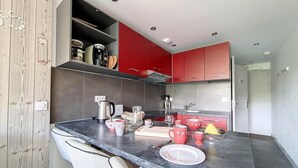 A modern kitchen with dark countertops, red cabinets, and a white chair. - Ski-in/ski-out & foot of the slopes, 5th floor, balcony, tv, 27m², Les Menuires (Les Menuires)