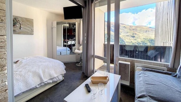 A hotel room with a bed, a small table with a remote control, and a view of a mountainous landscape. - Ski-in/ski-out & foot of the slopes, 5th floor, balcony, tv, 27m², Les Menuires (Les Menuires)