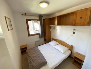 A bedroom with a single bed, wooden headboard, bedside tables, a window with curtains, and built-in wooden cabinets.