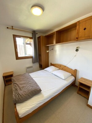 A single bed with a wooden headboard, a window with a view of buildings, and a ceiling light fixture. - 200m from ski slopes, 4th floor, view mountain, balcony, tv, 31m², Superdévoluy (Le Dévoluy)