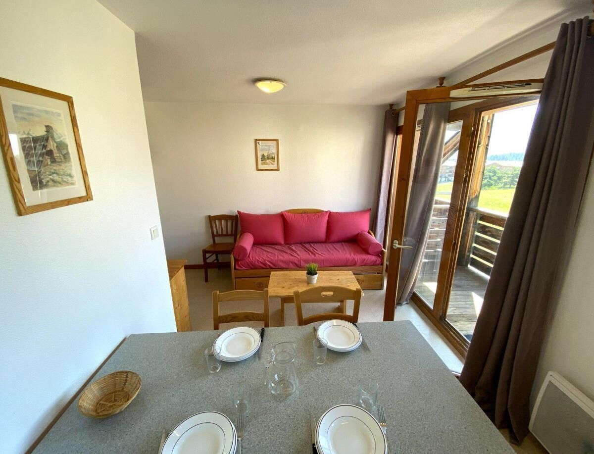 Un coin repas avec une table dressée pour deux personnes, un canapé rouge et une vue à travers une porte vitrée.