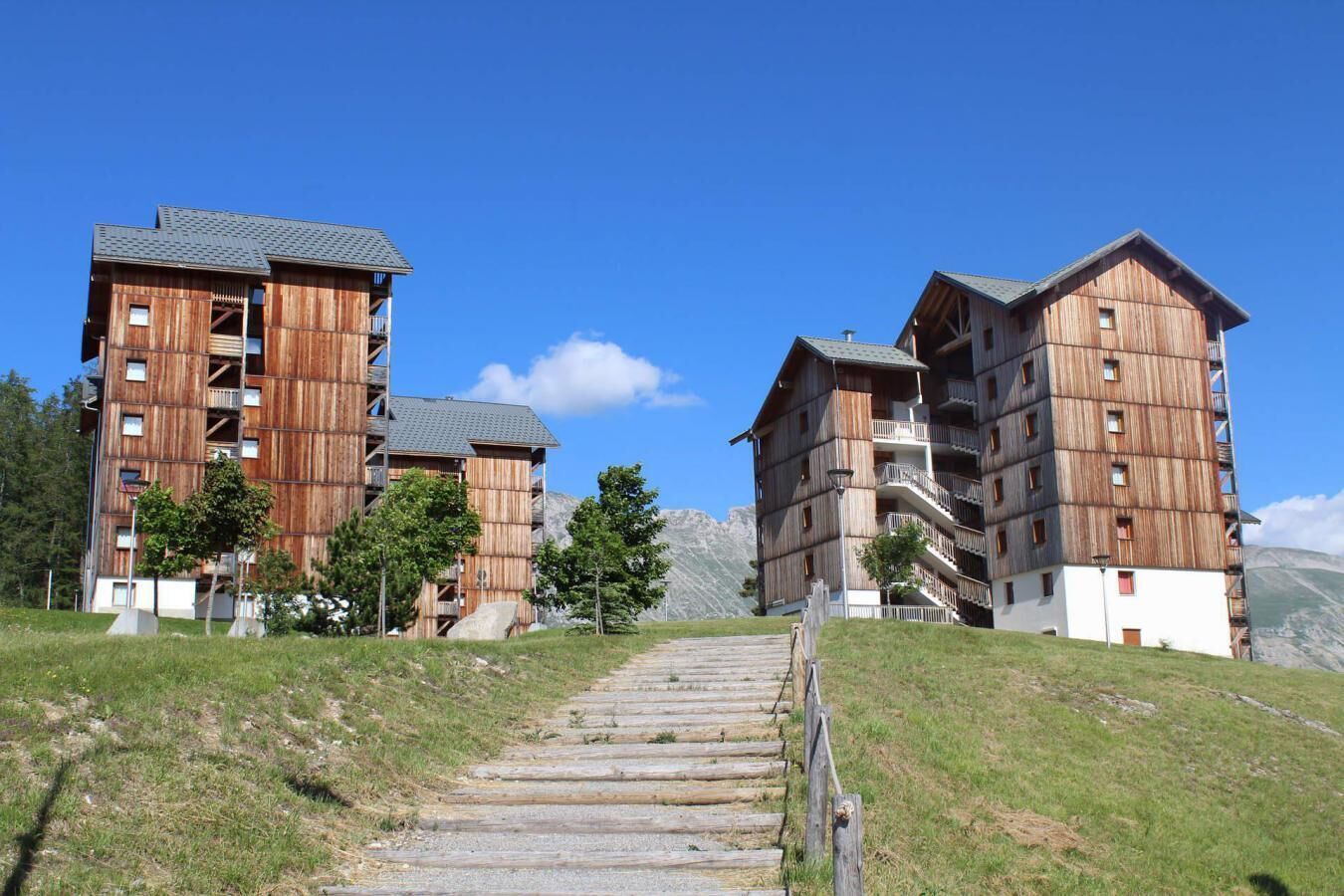 Ein mehrstöckiges Holzgebäude mit Balkonen und einer Treppe, die dazu führt, vor einer Bergkulisse.