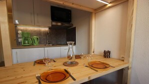Een houten eettafel, gedekt met oranje borden, bestek en een glazen karaf.