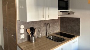 Een kleine keuken met witte kastjes, een roestvrijstalen spoelbak, een magnetron en een houten aanrecht.