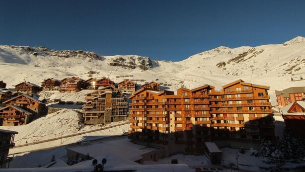 Een besneeuwde stad aan de voet van een berg, met houten gebouwen en een skipiste.