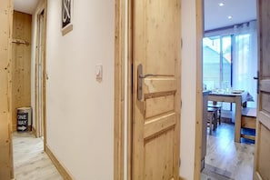 Um corredor com uma porta de madeira que dá para um quarto com uma mesa de jantar e cadeiras.