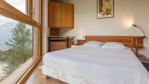 Een slaapkamer met een groot bed, een houten hoofdeinde, een nachtkastje, een lamp, een kledingkast en een raam met uitzicht op bomen en bergen.