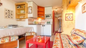 Een gezellige woonkamer met een bank, een eettafel en een keukenhoek met een magnetron.