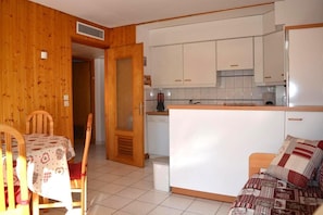 A compact kitchen with white cabinets, a wooden dining table with a patterned tablecloth, and a sofa with a patterned throw. - 50m from resort center, floor -1, view mountain, balcony, tv, 31m², Le Grand Bornand (Le Grand-Bornand)
