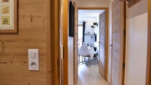 Un couloir étroit aux murs en bois, une porte blanche sur la droite et un coin repas visible à travers une porte ouverte au fond.
