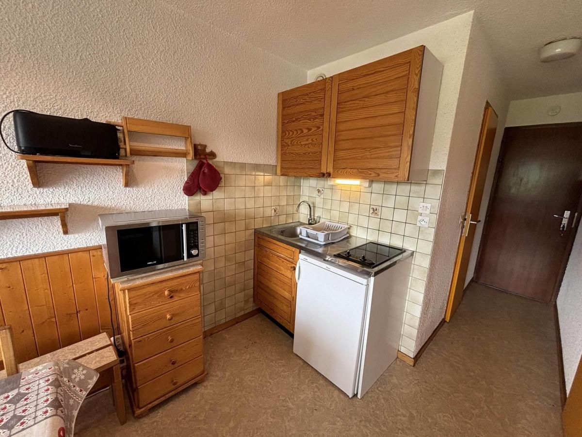 A compact kitchen with wooden cabinets, a microwave, a sink, and a small refrigerator.