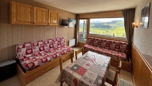 A cozy room with a sofa set, a table, and a view of a green landscape through a window. - 200m from ski slopes, 4th floor, view ski slopes, balcony, tv, ski locker, 18m², Les Saisies (Les Saisies)