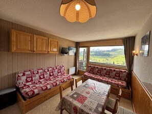 A cozy room with a sofa set, a table, and a view of a green landscape through a window.