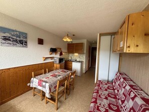 A compact kitchen with wooden cabinets, a dining table with chairs, and a small refrigerator.