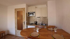 A compact kitchen with a microwave, stove, and sink. A dining table is set with plates, cutlery, and glasses. - 150m from ski slopes, 3rd floor, balcony, tv, 25m², Serre Chevalier (Briançon)