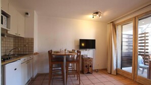 A compact kitchen with a dining table and chairs, a TV, and a sliding glass door to a balcony. - 150m from ski slopes, 3rd floor, balcony, tv, 25m², Serre Chevalier (Briançon)