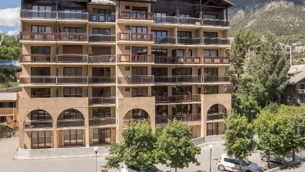 A multi-story hotel with balconies, arched windows, and a mountainous backdrop. - 150m from ski slopes, 3rd floor, balcony, tv, 25m², Serre Chevalier (Briançon)