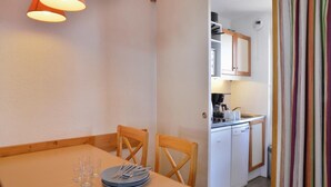 A dining area with a table set for four, wooden chairs, and a kitchen area with white appliances. - 100m from ski slopes, 1st floor, balcony, tv, 23m², La Plagne (La Plagne)