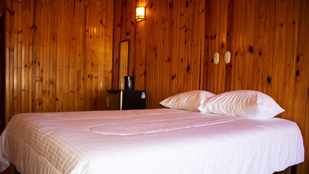 Una cama individual con ropa de cama blanca en una habitación con paredes de madera y una mesita con un hervidor.
