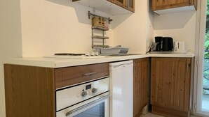 A compact kitchen with wooden cabinets, a white countertop, a built-in oven, and a small refrigerator.