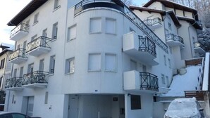 A multi-story building with balconies, a staircase, and a car covered in snow.