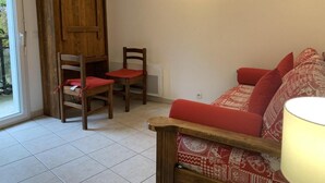 A cozy living room with a wooden door, two wooden chairs with red cushions, a red sofa with patterned cushions, and a wooden bench.