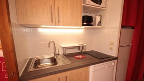 Une cuisine compacte avec des meubles en bois, un évier en acier inoxydable, un four à micro-ondes et un lave-vaisselle blanc.