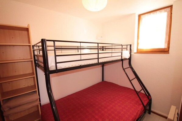 A bunk bed with a red mattress, a wooden shelf unit, and a window with light coming through. - 100m from shops, Ground floor, view ski slopes, terrace, tv, ski locker, 23m², Les Saisies (Les Saisies)