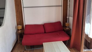 Una habitación pequeña y acogedora con un sofá rojo, dos mesitas de noche con lámparas y una ventana con cortinas.