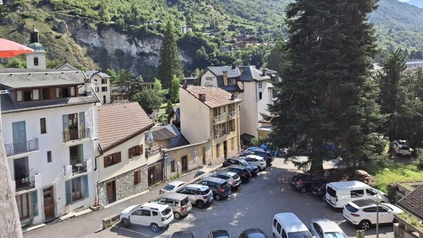 Un hotel con un patio central, rodeado de edificios con balcones y un paisaje montañoso de fondo.
