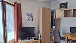 Una habitación compacta con una televisión sobre un aparador de madera, un escritorio con una silla y un armario.