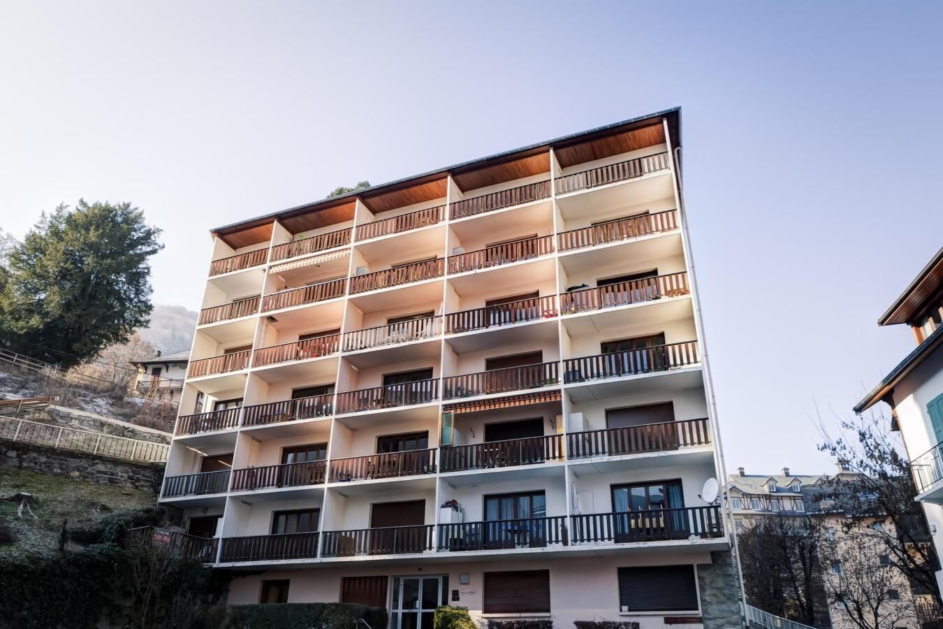 A multi-story building with balconies, a stone wall, and a clear sky.