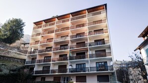 Un edificio de varios pisos con balcones, un muro de piedra y cielo despejado.
