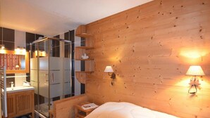 Una habitación con pared de madera, una cama, una mesita de noche, un espejo, un armario y cabina de ducha.