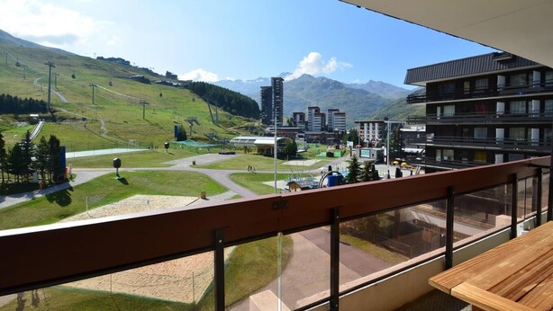 Un balcón con vistas a una estación de esquí, que incluye un telesilla, edificios y montañas.