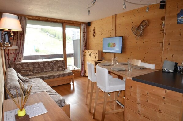 Un acogedor interior de cabaña con una zona de comedor de madera, un sofá con cojines estampados y un televisor montado en la pared.