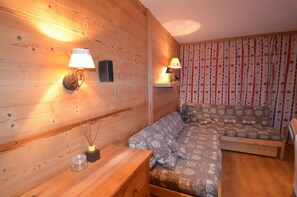 Una habitación acogedora con paredes de madera, un sofá con cojines estampados con corazones y dos lámparas fijadas a la pared.