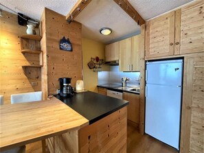A compact kitchen with wooden cabinets, a black countertop, and a white refrigerator. - 10m from ski slopes, 3rd floor, balcony, tv, 36m², Les Menuires (Les Menuires)