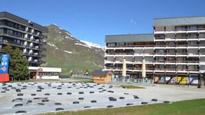 Un hotel de varios pisos, con una montaña al fondo y un estacionamiento con neumáticos.