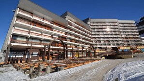 Un hotel de varios pisos con balcones, un telesilla y suelo cubierto de nieve.