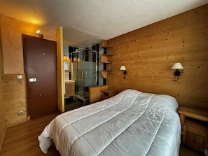 A bedroom with a large bed, wooden walls, a wooden door, and a small bedside table with a lamp. - 10m from ski slopes, 3rd floor, balcony, tv, 36m², Les Menuires (Les Menuires)