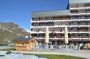 A multi-story hotel with balconies, a wooden cabin-like structure in front, and a mountain in the background. - 10m from ski slopes, 3rd floor, balcony, tv, 36m², Les Menuires (Les Menuires)