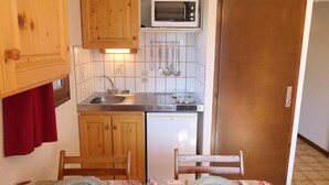 A compact kitchen with wooden cabinets, a microwave, a sink, and a small refrigerator. - Ground floor, balcony, parking, tv, 23m², Saint Gervais (Saint-Gervais-les-Bains)