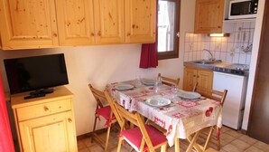 A compact kitchen with wooden cabinets, a microwave, and a dining table set for four. - Ground floor, balcony, parking, tv, 23m², Saint Gervais (Saint-Gervais-les-Bains)