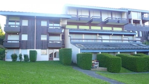 Un moderno edificio residencial de varios pisos con balcones, una entrada cubierta y un césped bien cuidado.