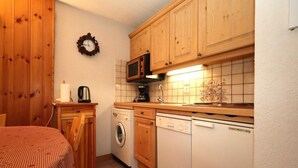A compact kitchen with wooden cabinets, a microwave, a washing machine, and a dishwasher.