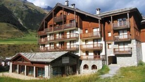 A multi-story hotel with balconies, set against a mountainous backdrop.