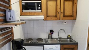 A compact kitchen with wooden cabinets, a microwave, a toaster, a coffee maker, a dishwasher, and a sink.