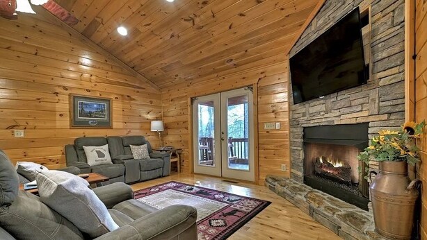 Interior acogedor de una cabaña con chimenea de piedra, paredes de madera, un sofá y un ventanal grande.